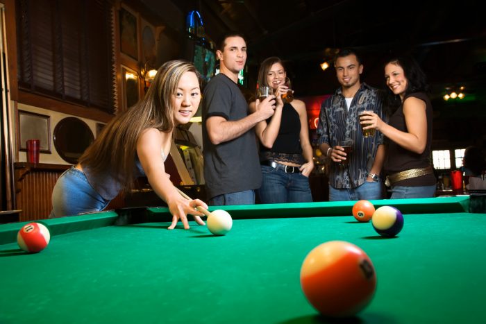 Young woman playing pool with group of friends in pub, Central Coast NSW