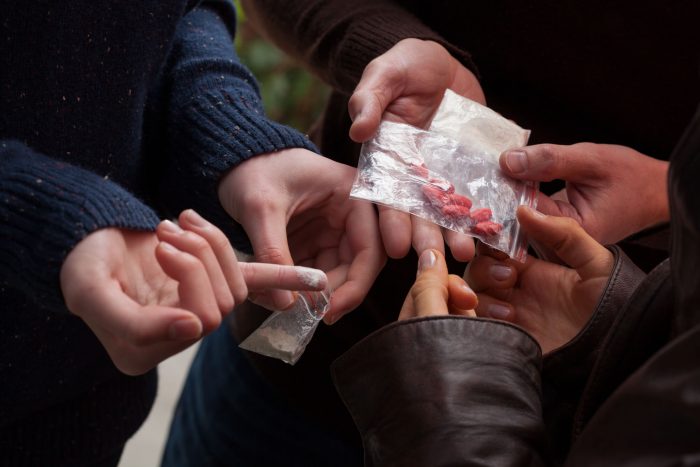 Three pairs of hands holding illicit drugs