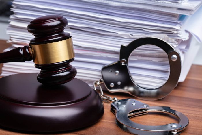Close-up Of Gavel And Handcuffs Near Stacked Paper On Wooden Table